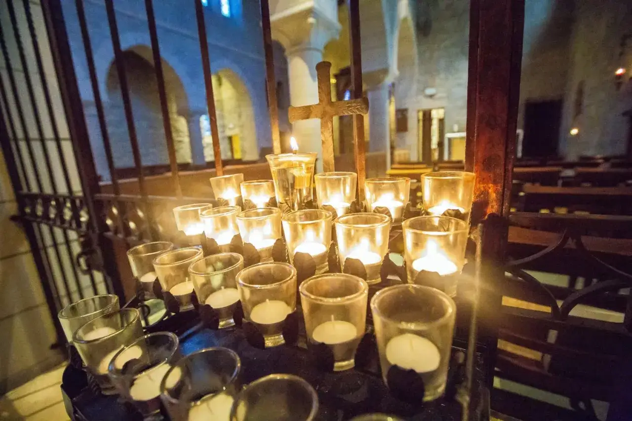 Candles glow in a church, a quiet scene of praying at 3am in the morning. A wooden cross stands behind the votive lights.