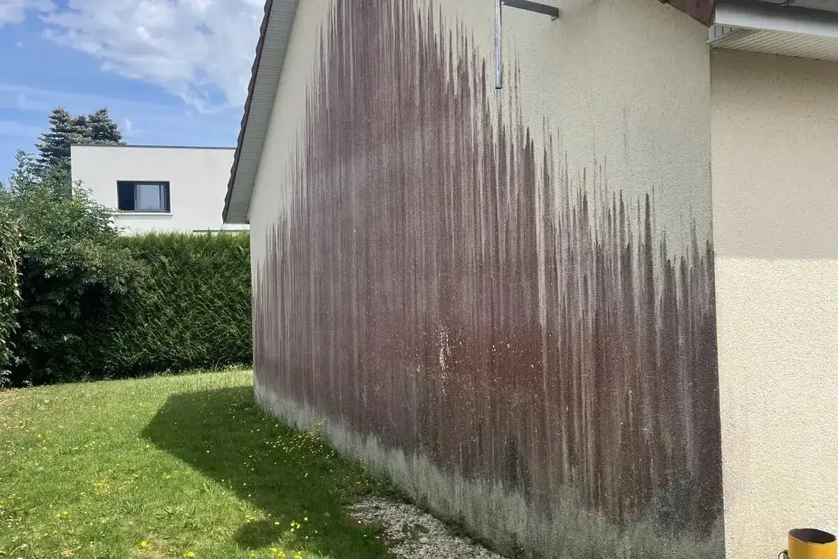 Traces sombres sur un mur ext&eacute;rieur, probablement dues &agrave; des algues rouges et &agrave; l'eau de javel utilis&eacute;e pour le nettoyage.