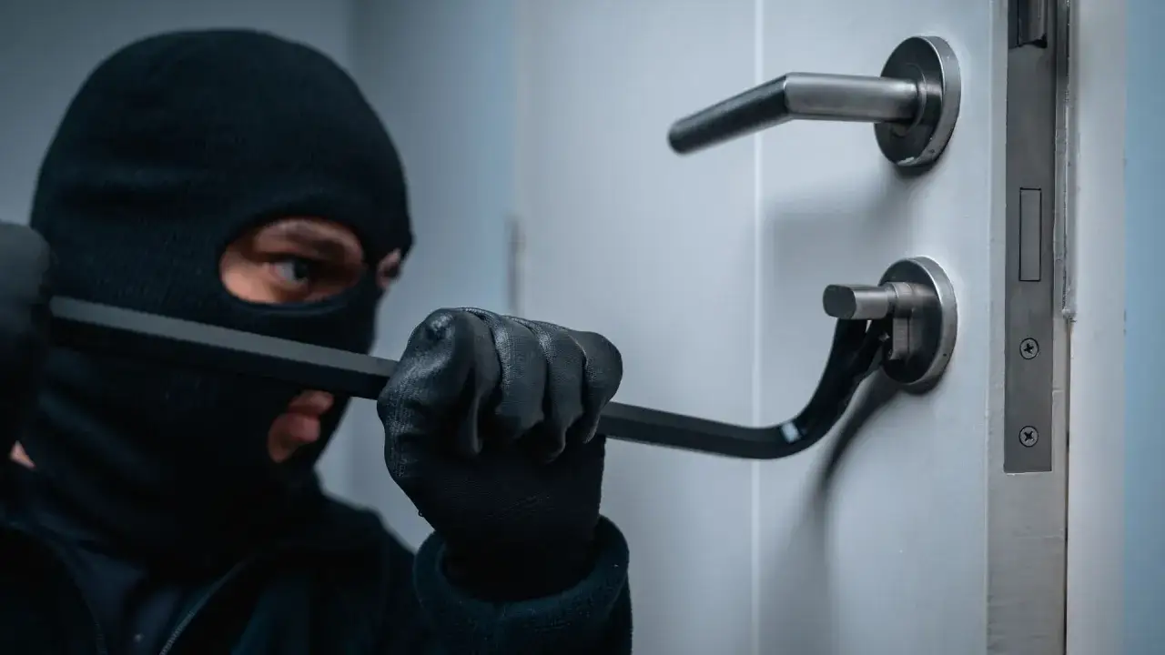 Cambrioleur masqué forçant une porte. Une effraction qui pourrait affecter l'assurance propriétaire ou locataire.
