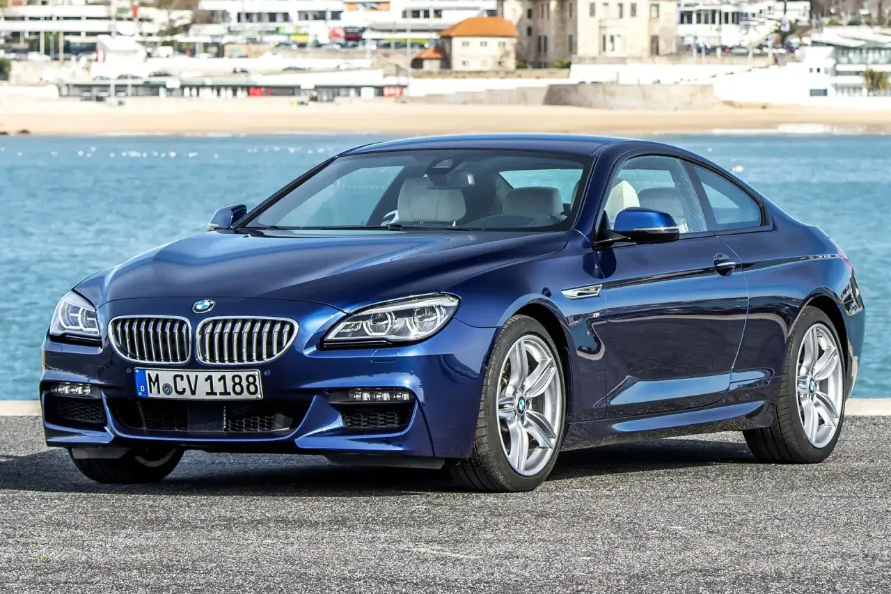 Granatowe BMW 640d coupe z jasnym wnętrzem stoi nad błękitnym morzem, w tle zabudowania nadbrzeżne.