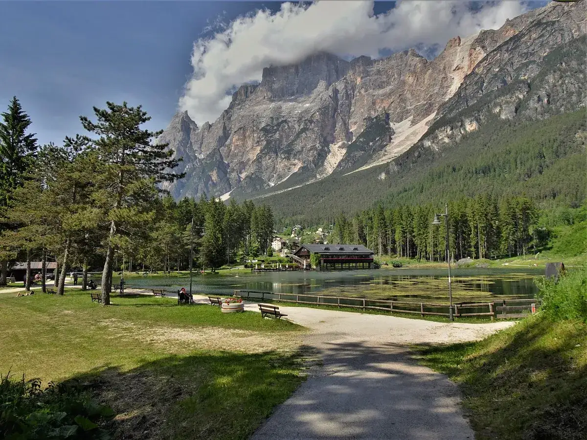 Un tranquillo lago di Mosigo incorniciato da imponenti montagne e una fitta foresta. Panchine e sentieri invitano a godersi il paesaggio.