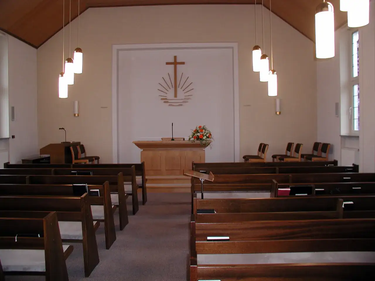 Interior of an apostolic church with wooden pews, a pulpit, and a cross symbol.