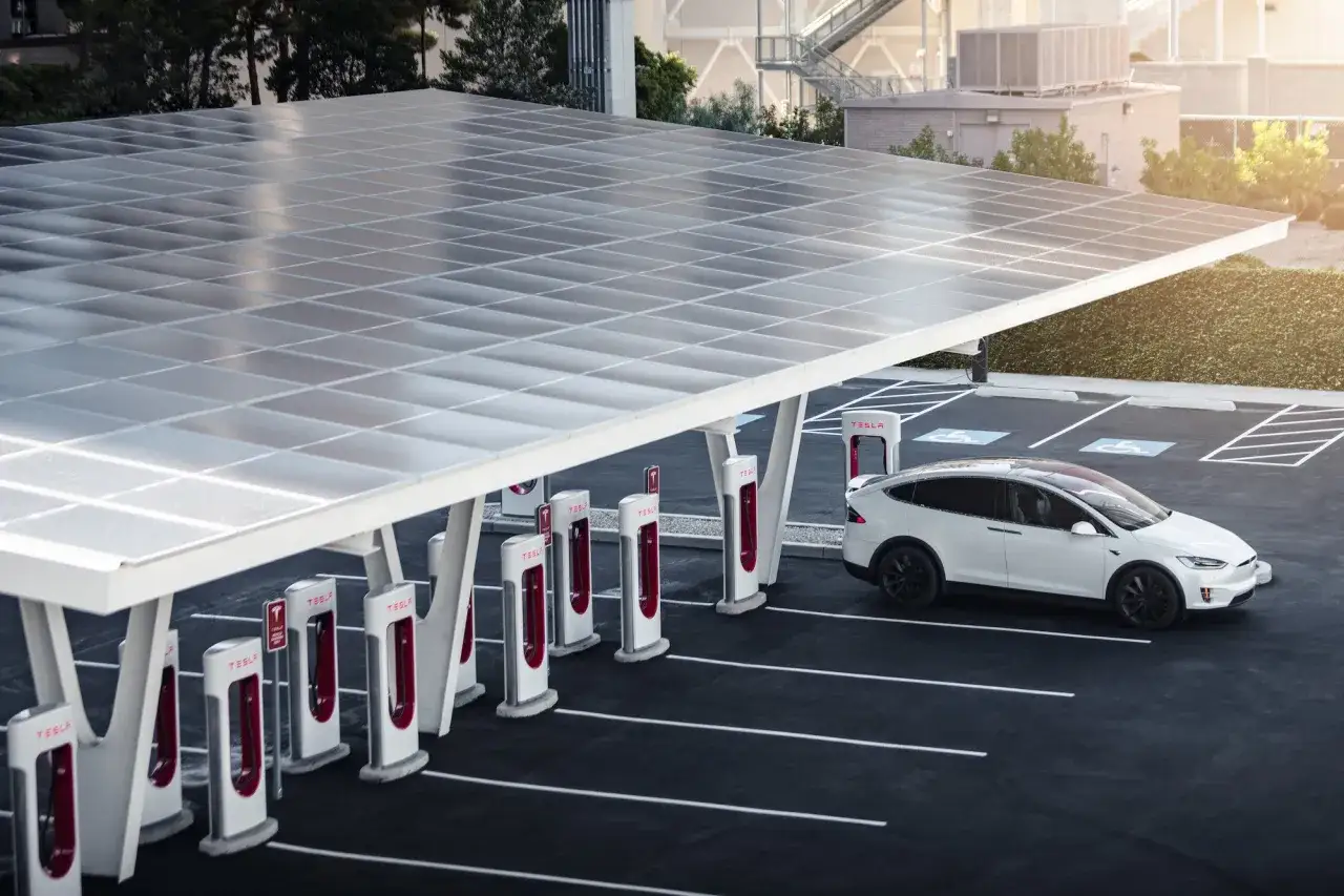 Biała Tesla X ładuje się na stacji Supercharger pod panelem słonecznym. Zastanawiasz się, ile kosztuje Tesla?