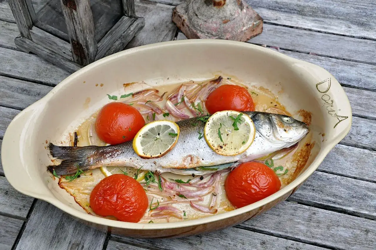 Un bar entier, prêt pour la cuisson au four, est présenté dans un plat avec des tomates, des oignons et des rondelles de citron.
