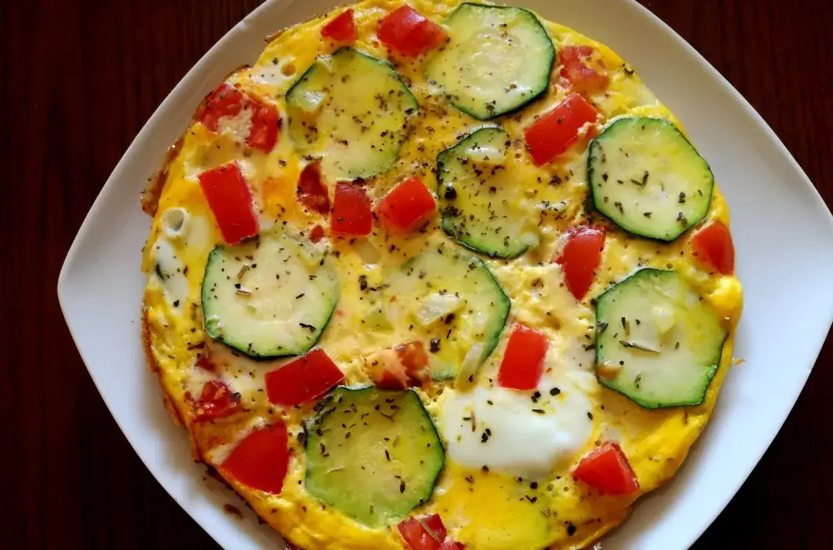Pyszny omlet z cukinią, pomidorami i ziołami, podany na białym talerzu.