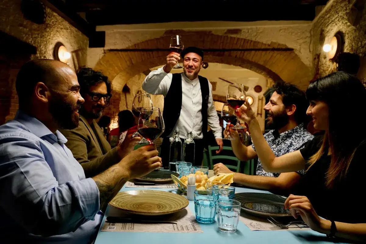 Brindisi in un ristorante in Sardegna. Un gruppo di amici festeggia con calici di vino rosso, godendosi l'atmosfera accogliente.