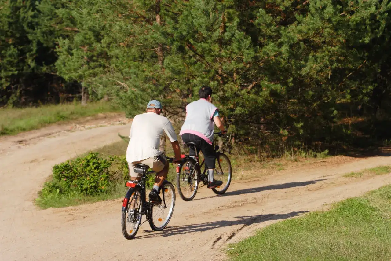 Dwie osoby na rowerach odkrywają najładniejsze trasy rowerowe na Mazowszu, jadąc piaszczystą drogą wśr&oacute;d drzew.