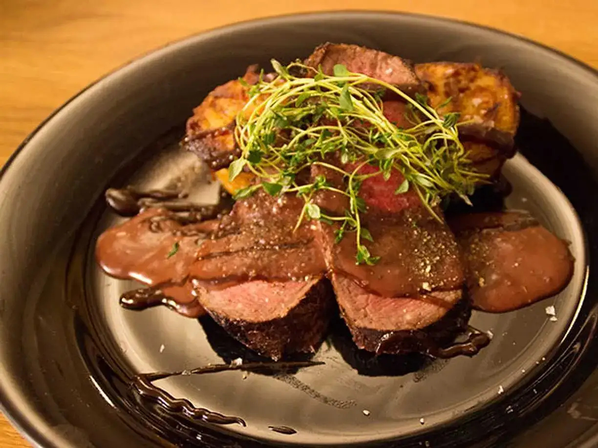 Saftig ryggbiff i ugn, skivad och serverad med en mustig sås, rostade potatisar och färska örter.