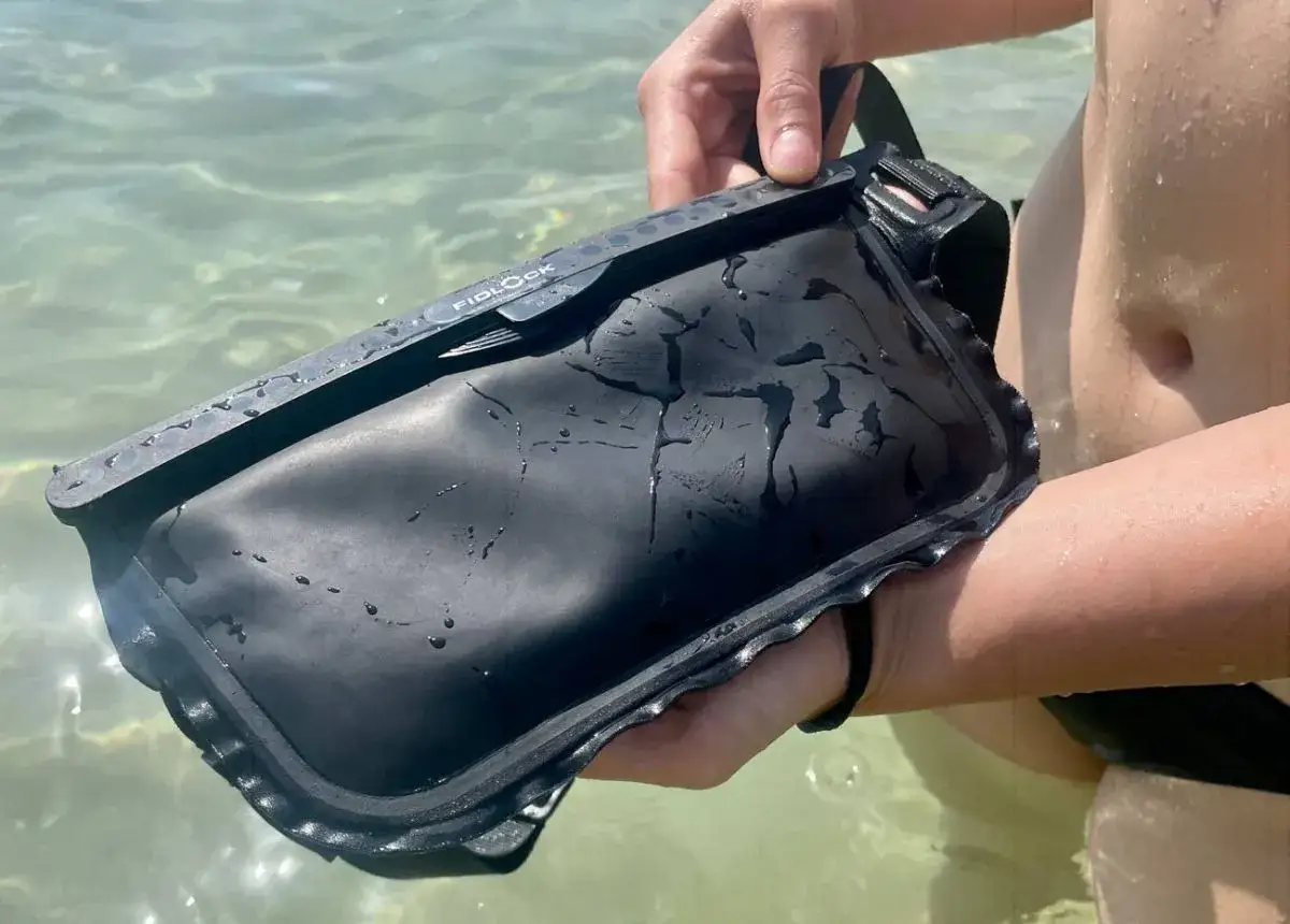 Schwarze wasserdichte Tasche mit Fidlock-Verschluss, die zeigt, was wasserdicht bedeutet. Perfekt f&uuml;r den Strand.