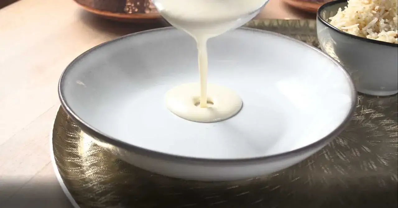 Cremige Béchamelsauce fließt in eine Schüssel. Daneben steht eine Schüssel mit Reis.