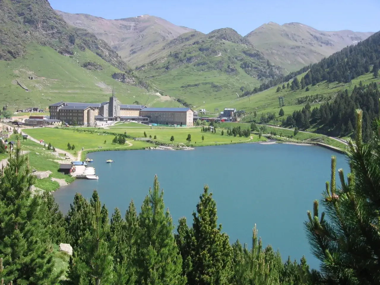 El **Valle de Nuria** se despliega con un lago turquesa, un santuario imponente y montañas verdes.