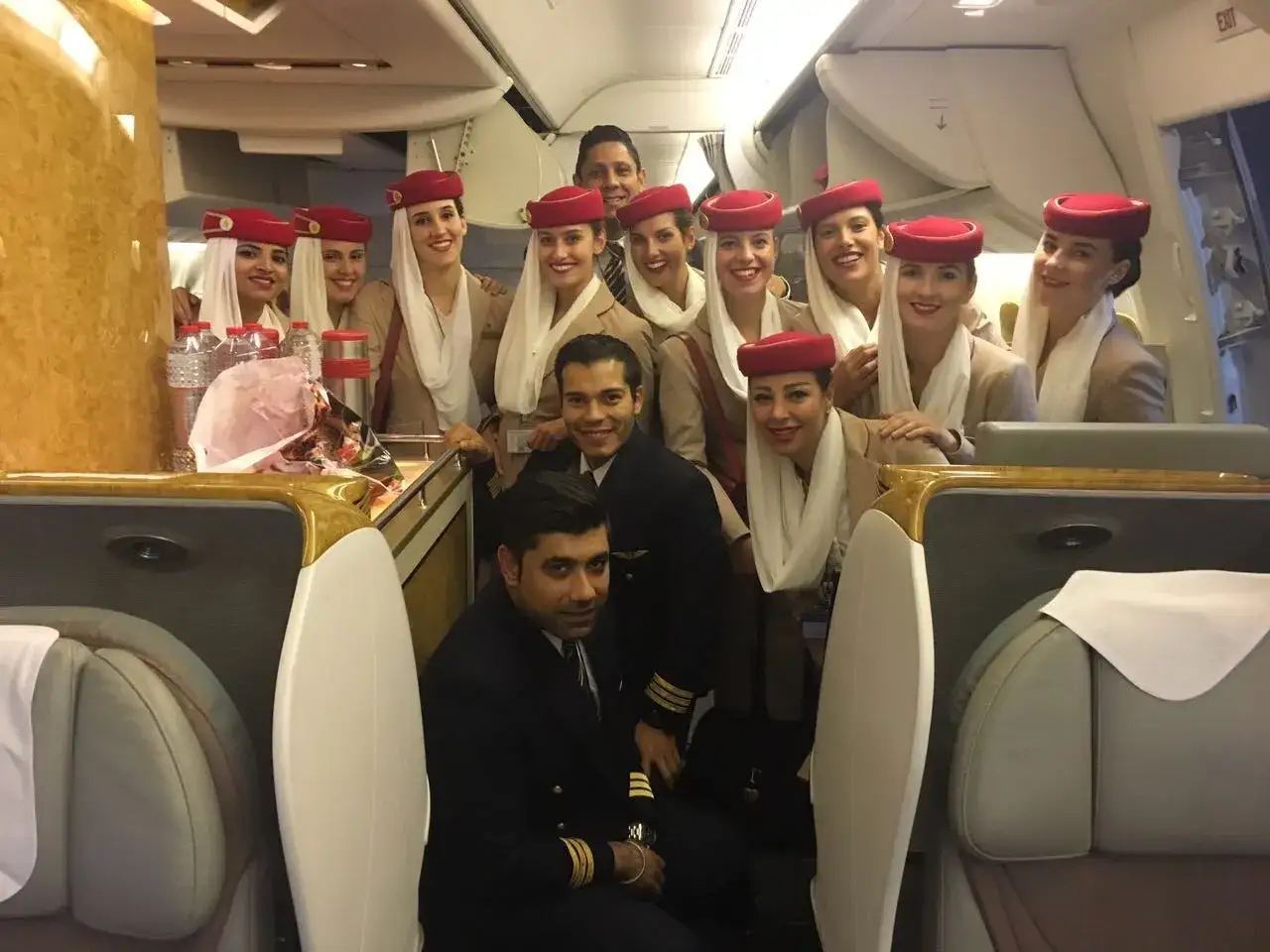 Uśmiechnięta załoga Emirates: pilot i stewardessy w charakterystycznych czerwonych beretach pozują do zdjęcia w luksusowym wnętrzu samolotu.