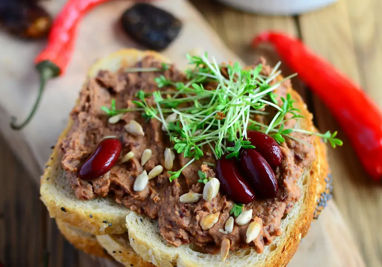 Pyszna pasta z czerwonej fasoli na chlebie, ozdobiona kiełkami i nasionami. Obok leżą papryczki chili.