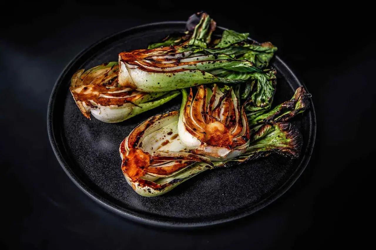 Gegrillter Pak Choi auf einem dunklen Teller, mit sch&ouml;nen Grillspuren und leicht welken Bl&auml;ttern.