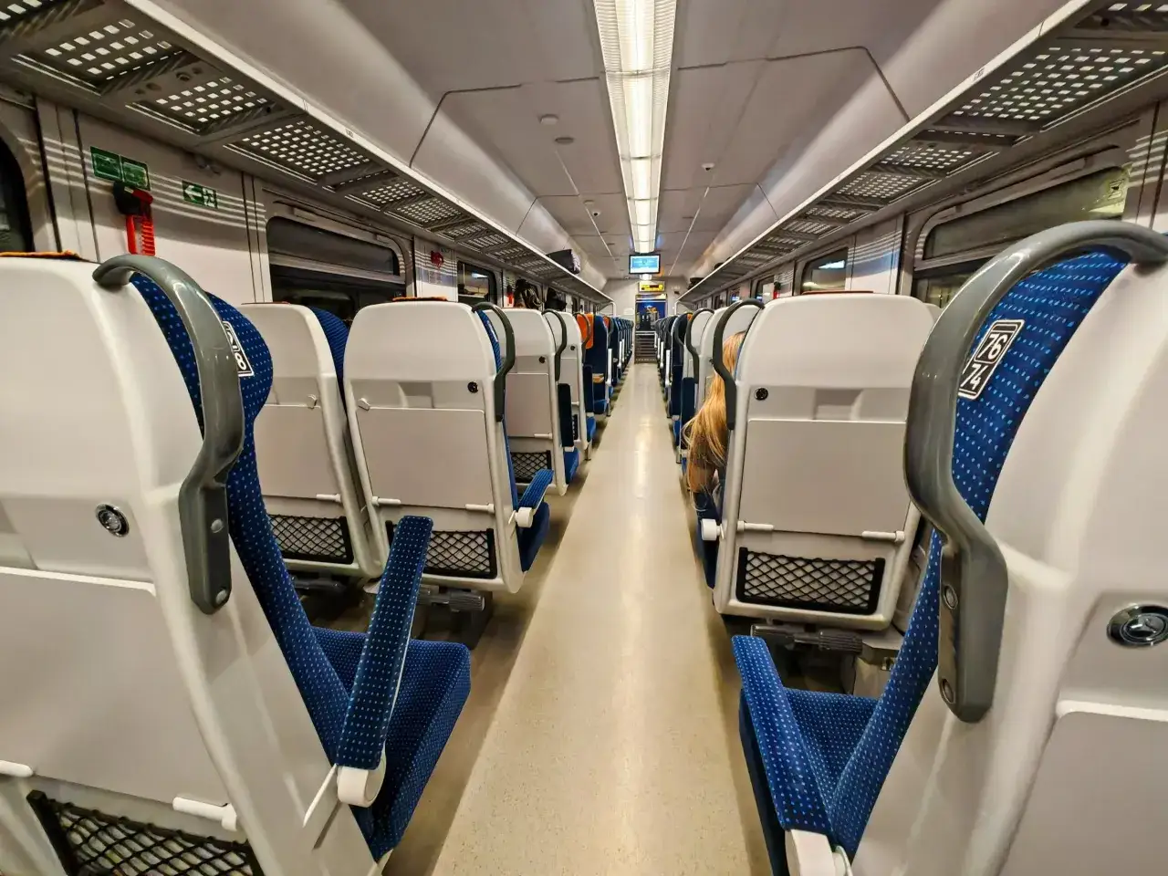 Wnętrze pociągu Pendolino, siedzenia w kolorze białym i niebieskim, gotowe do podróży z Poznania do Warszawy.