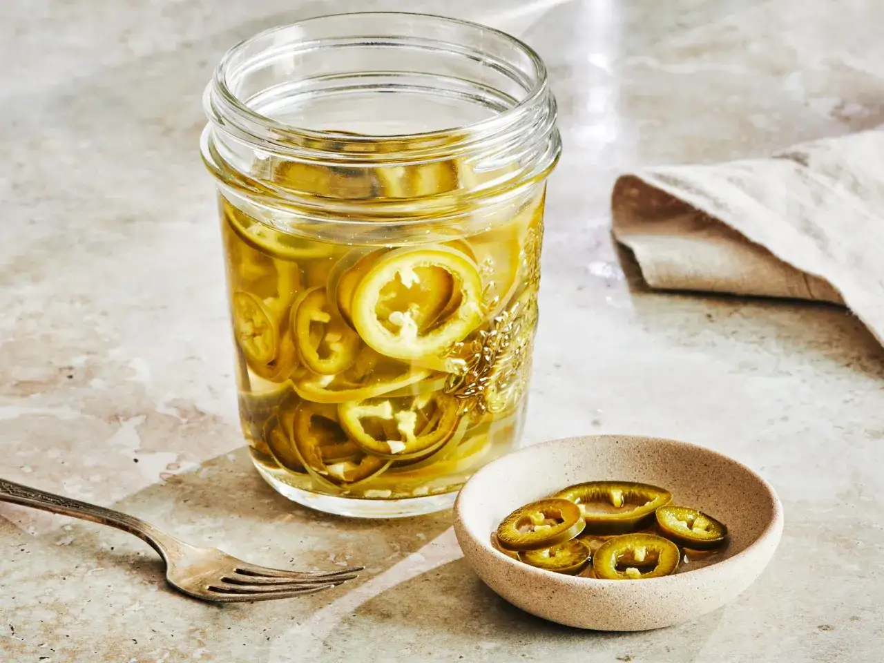 Un bocal rempli de rondelles de **pickles piment** et un petit bol avec quelques-unes. Une fourchette repose &agrave; c&ocirc;t&eacute;.