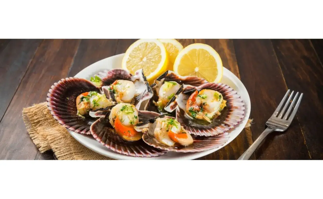 Zamburiñas a la plancha, servidas en sus conchas con limón y perejil, listas para disfrutar.