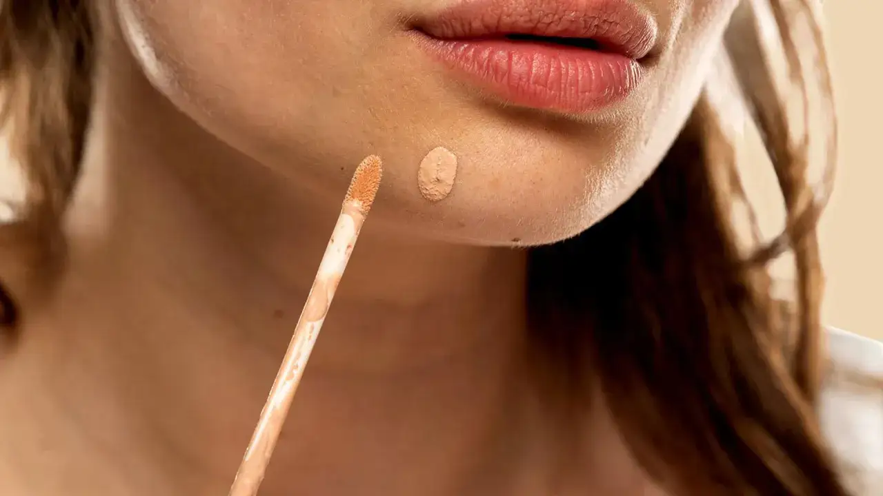 En applikator med concealer bredvid en liten klick av produkten på huden.