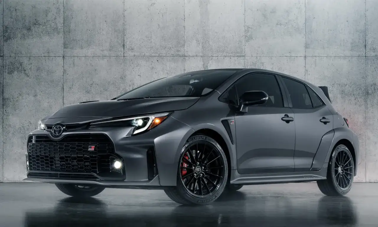 M&ouml;rkgr&aring; Toyota Corolla GR med sportiga detaljer, svarta f&auml;lgar och r&ouml;da bromsok, st&aring;r framf&ouml;r en betongv&auml;gg.