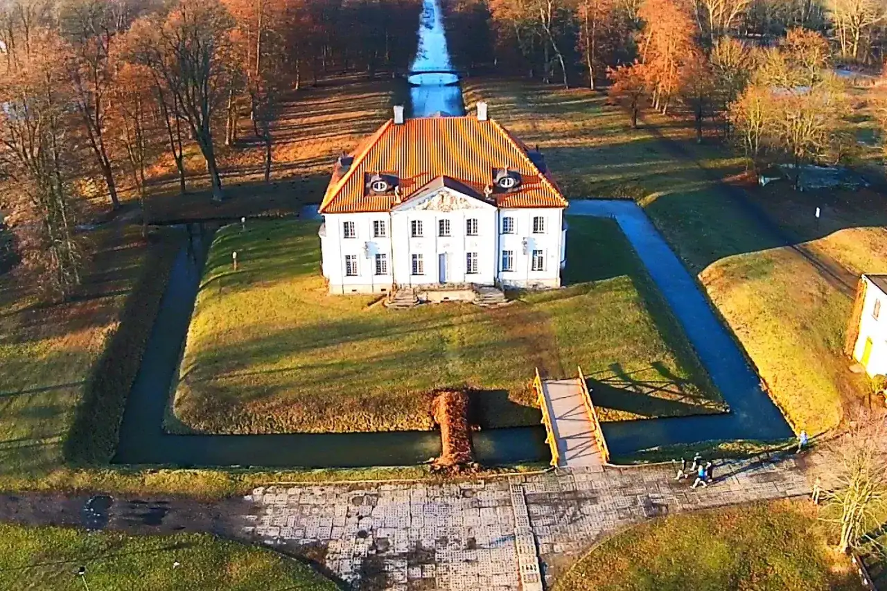 Pałac w Choroszczy otoczony fosą, z pomostem i aleją drzew.