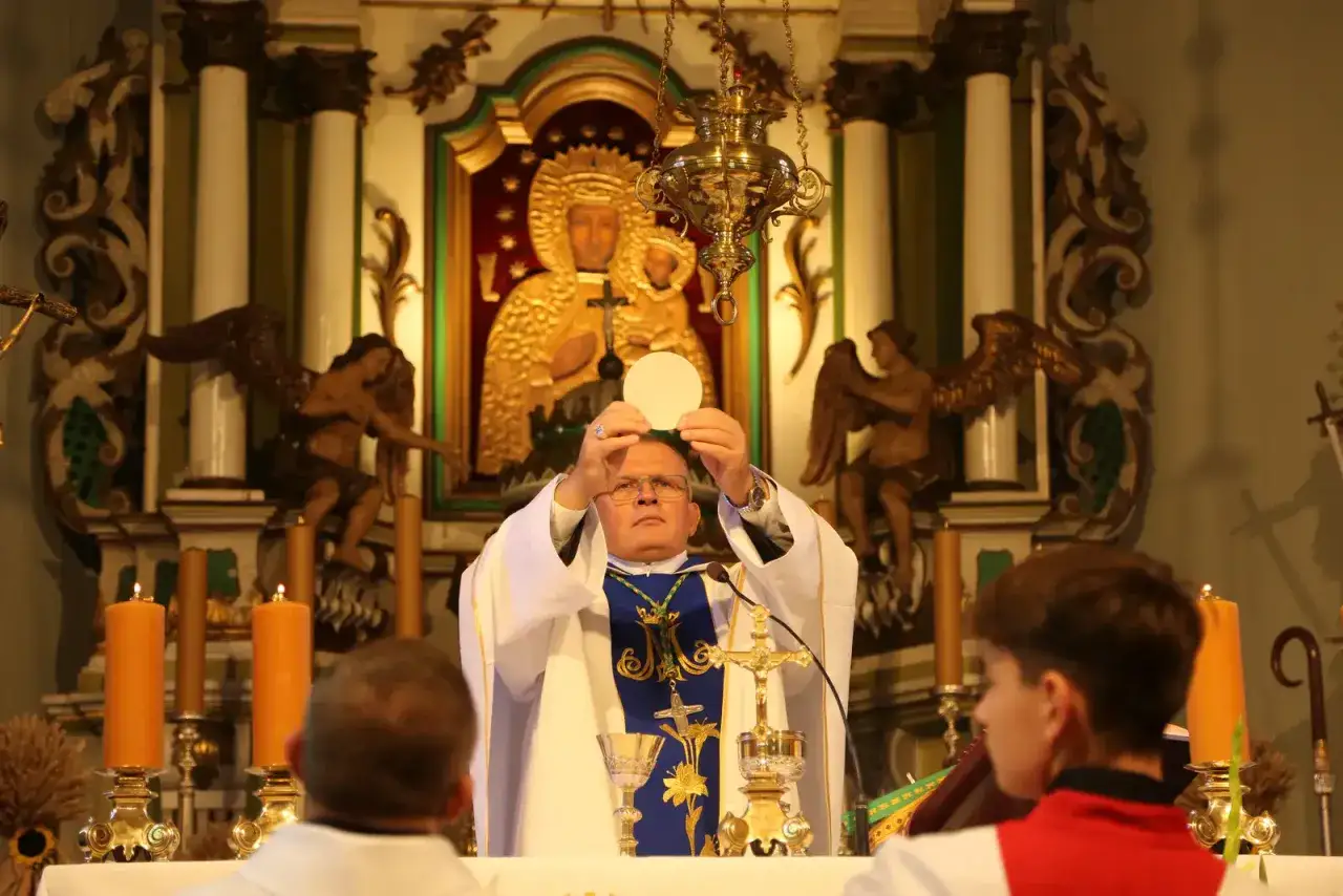 Kapłan podczas mszy bierzmowania podnosi hostię. W tle obraz Matki Boskiej i ozdobne rzeźby.
