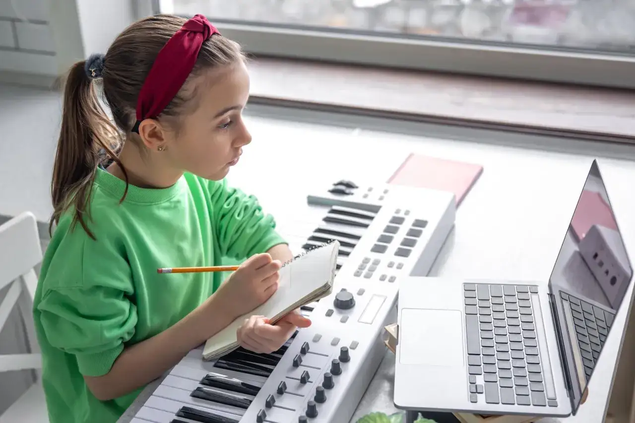 Jeune fille concentrée, elle apprend à jouer d'un instrument de musique, un clavier, en prenant des notes.