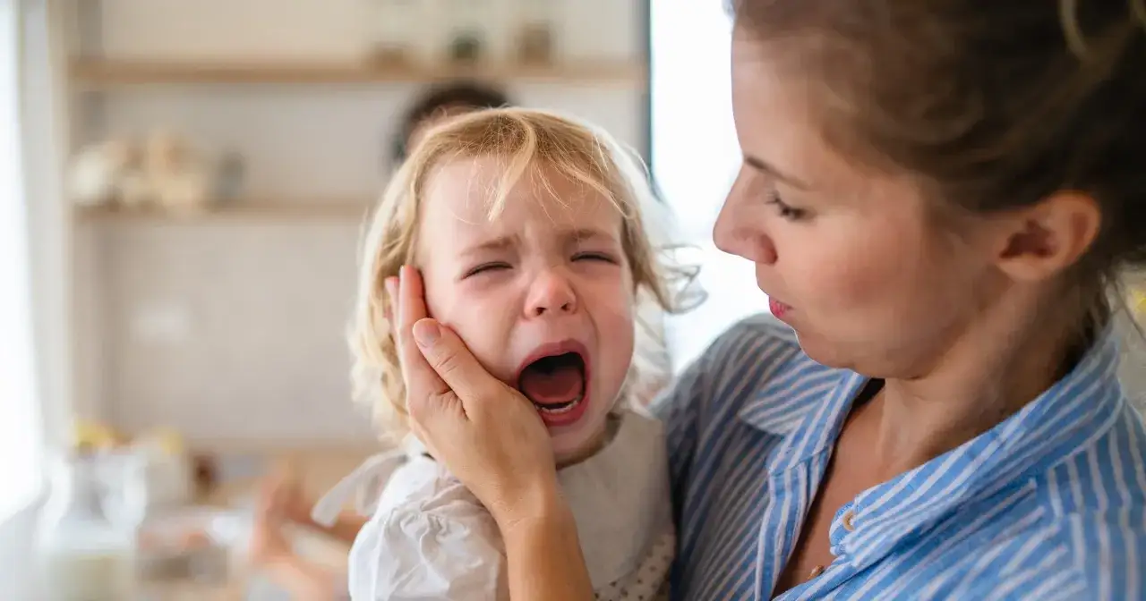 Małe dziecko płacze, przeżywając lęk separacyjny, gdy mama próbuje je uspokoić.