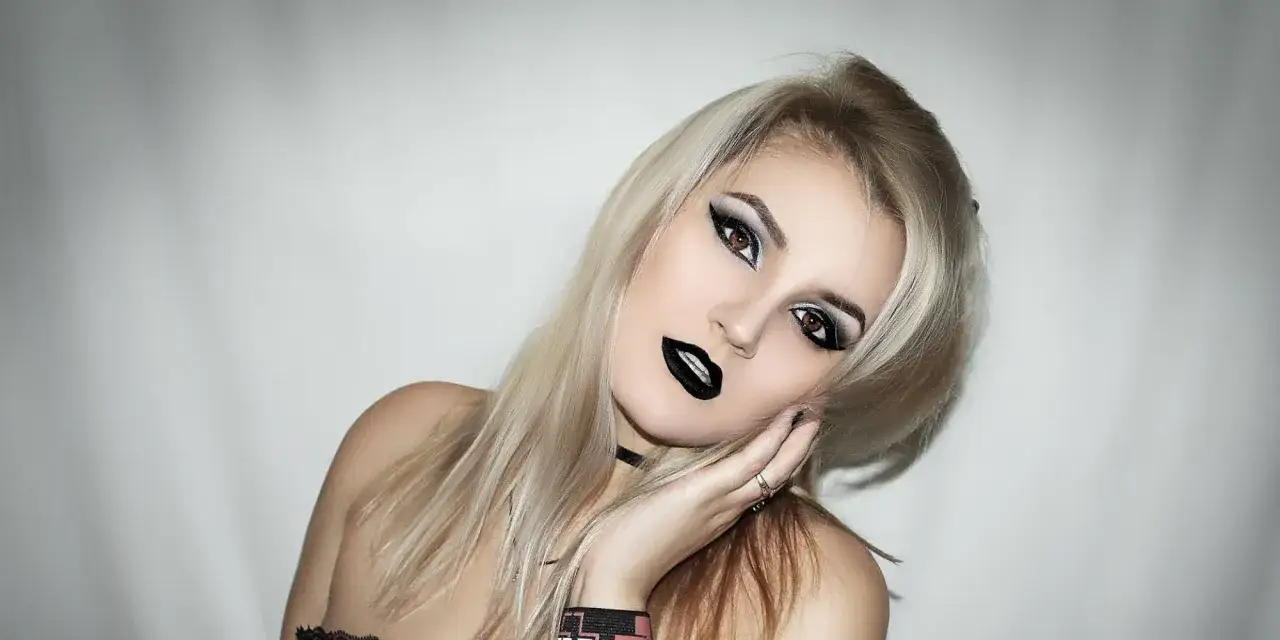 Une jeune femme avec une coiffure rock, des cheveux blonds d&eacute;color&eacute;s, un maquillage audacieux avec des yeux charbonneux et des l&egrave;vres noires.