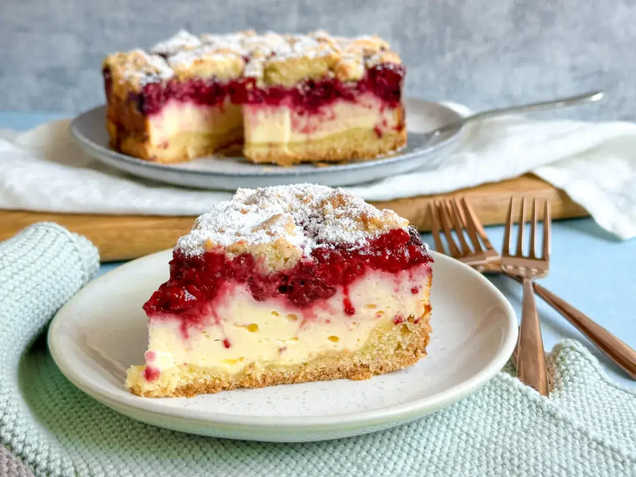 Ein saftiges Stück Quarkkuchen ohne Boden mit Himbeeren und Streuseln, bestäubt mit Puderzucker.