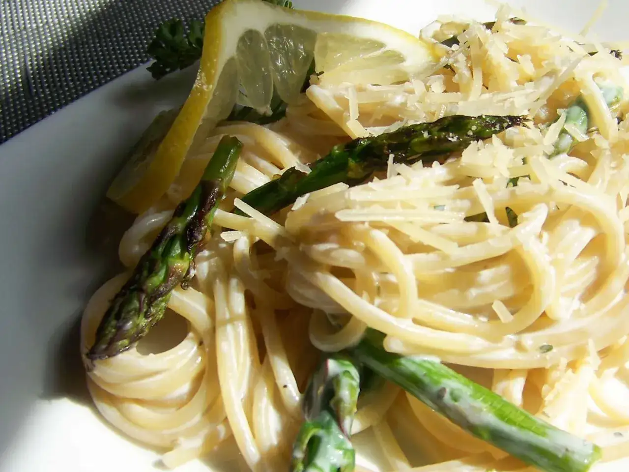 Tagliatelle ze szparagami, posypane parmezanem i ozdobione plasterkami cytryny. Pyszne danie na wiosnę.