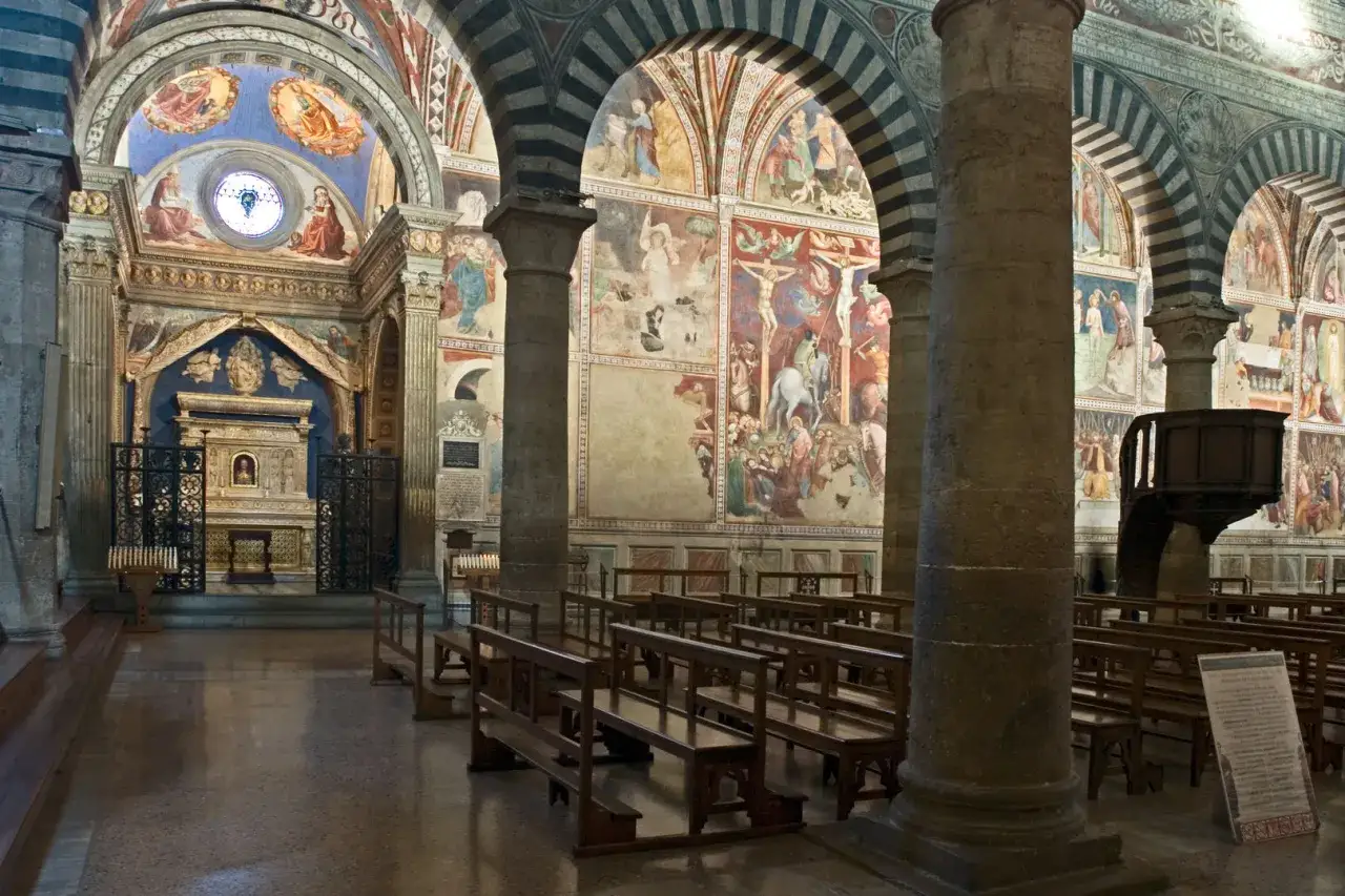 Interno del Duomo di San Gimignano, con affreschi medievali e panche di legno.