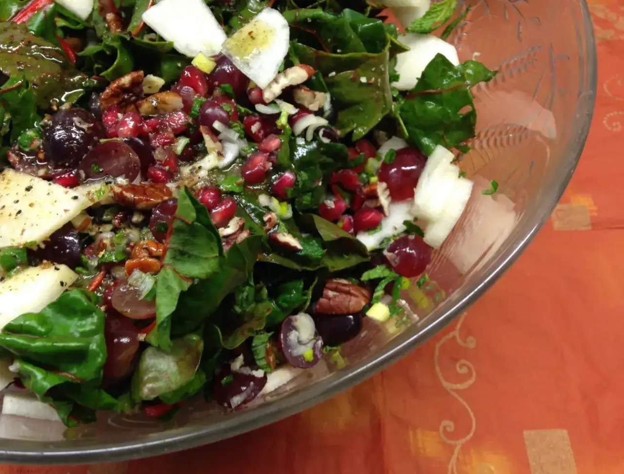 Bunter Salat mit Mangold, Trauben, Granatapfelkernen und Nüssen in einer Glasschüssel.