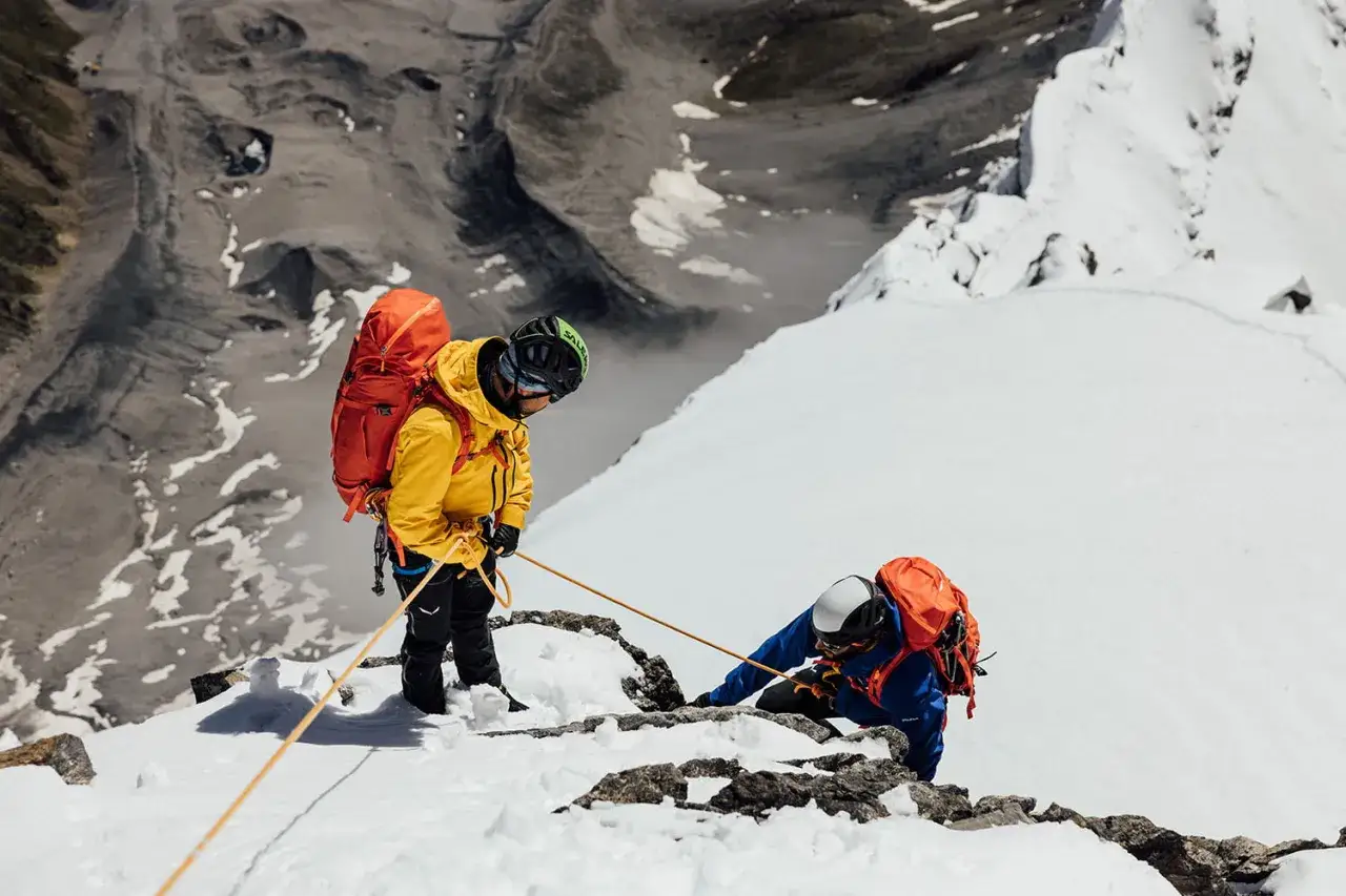 Dw&oacute;ch alpinist&oacute;w w sprzęcie Salewa wspina się po ośnieżonym zboczu. Salewa to firma znana z odzieży i sprzętu g&oacute;rskiego.
