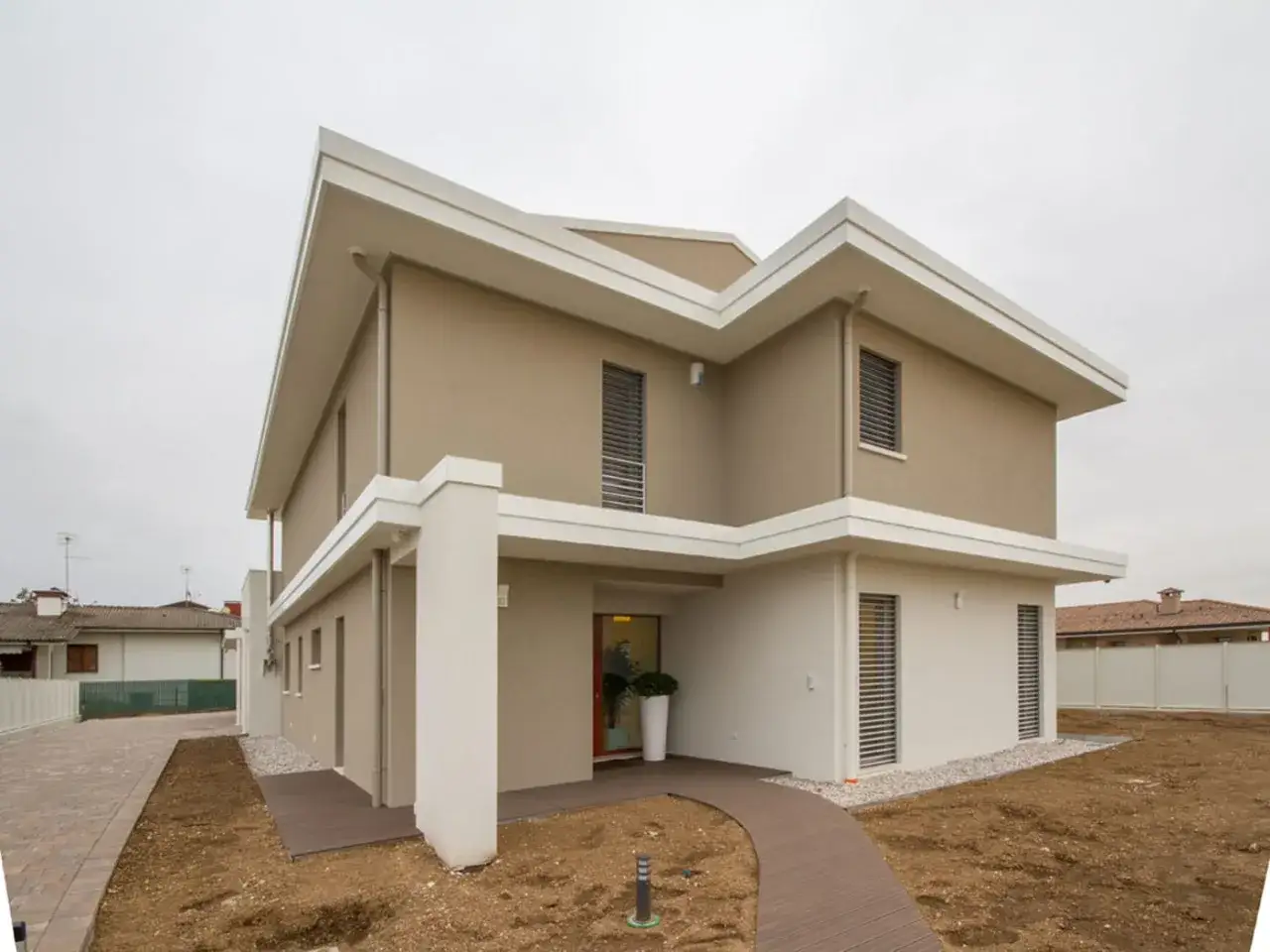 Casa moderna con esterno color sabbia tortora, con dettagli bianchi e un vialetto in legno.