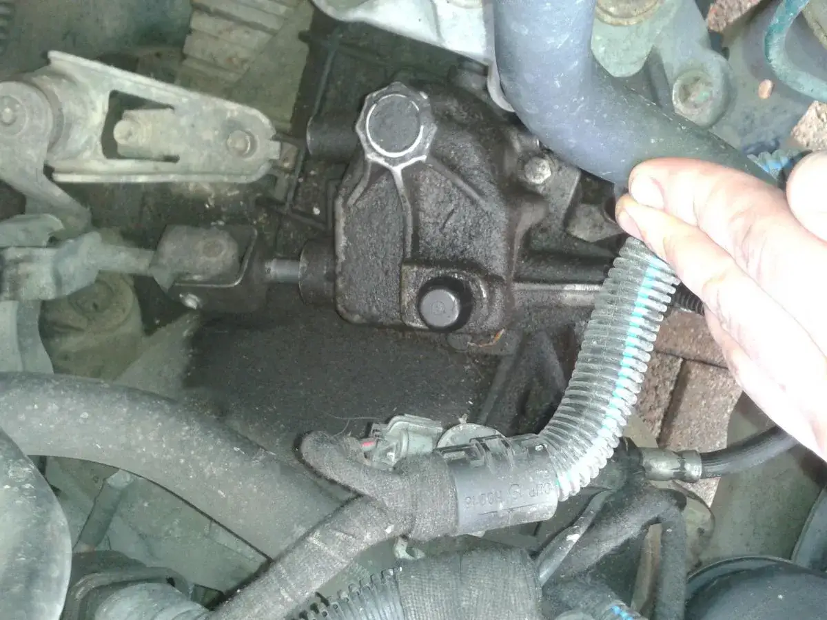Widoczny jest mechanizm skrzyni biegów z elementem odpowietrznik skrzyni biegów. Dłoń mechanika sprawdza stan węża.