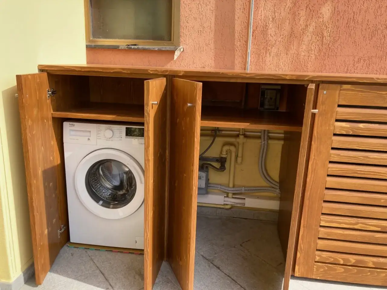 Mobiletti in legno per nascondere lavatrice in bagno, con tubi e contatore a vista.