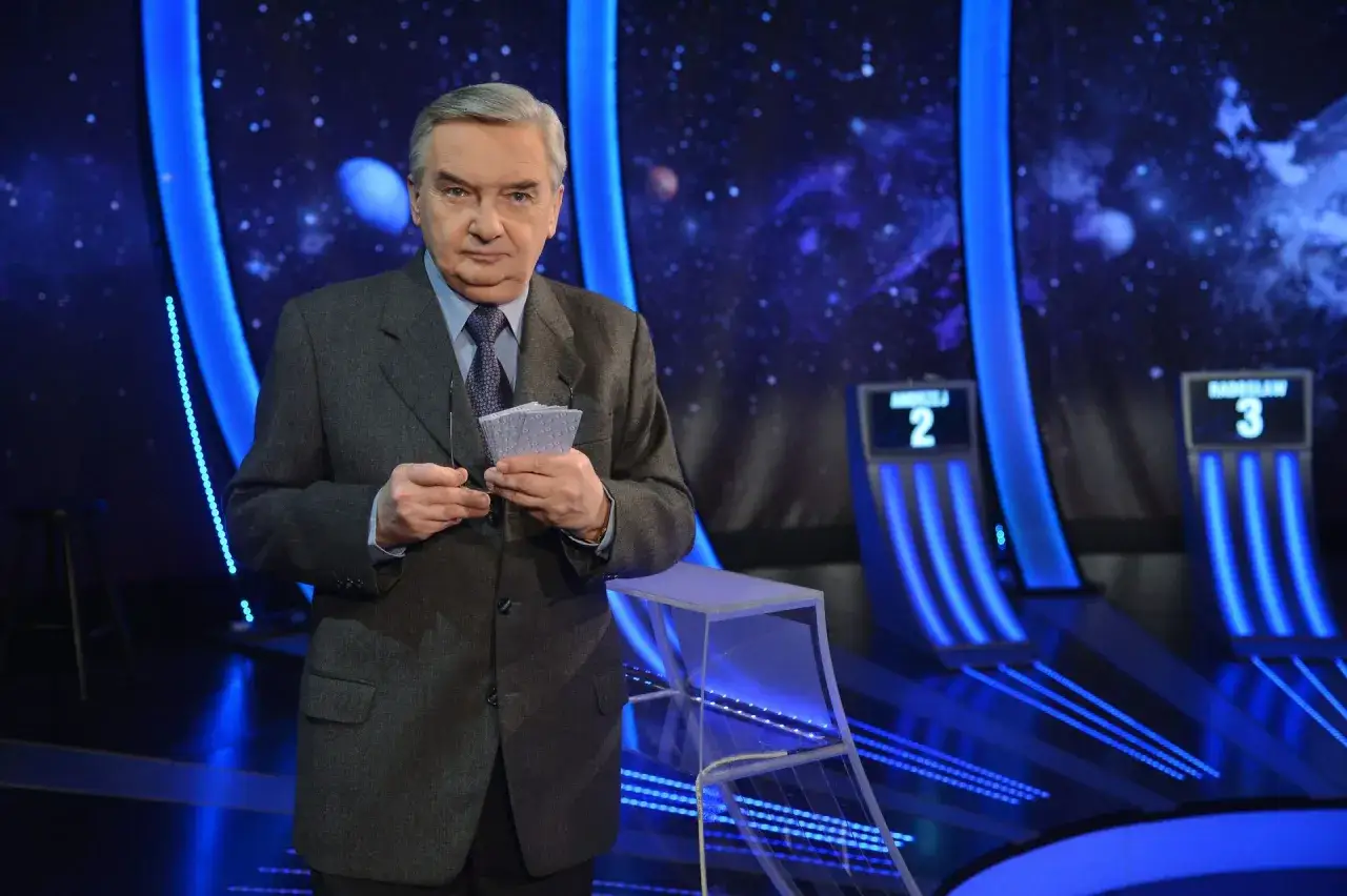 Starsza osoba w garniturze trzyma karty z napisem