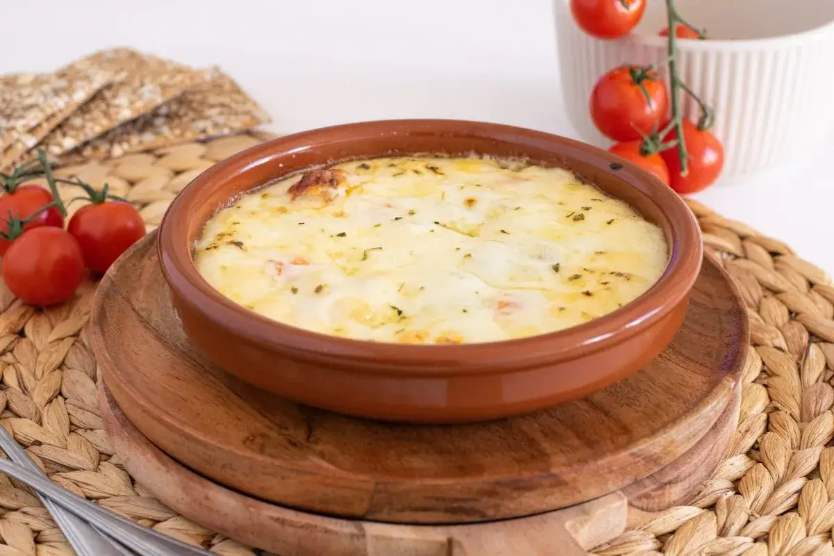 Un delicioso provolone al horno burbujeante, servido en una cazuela de barro, acompañado de tomates cherry y galletas crujientes.