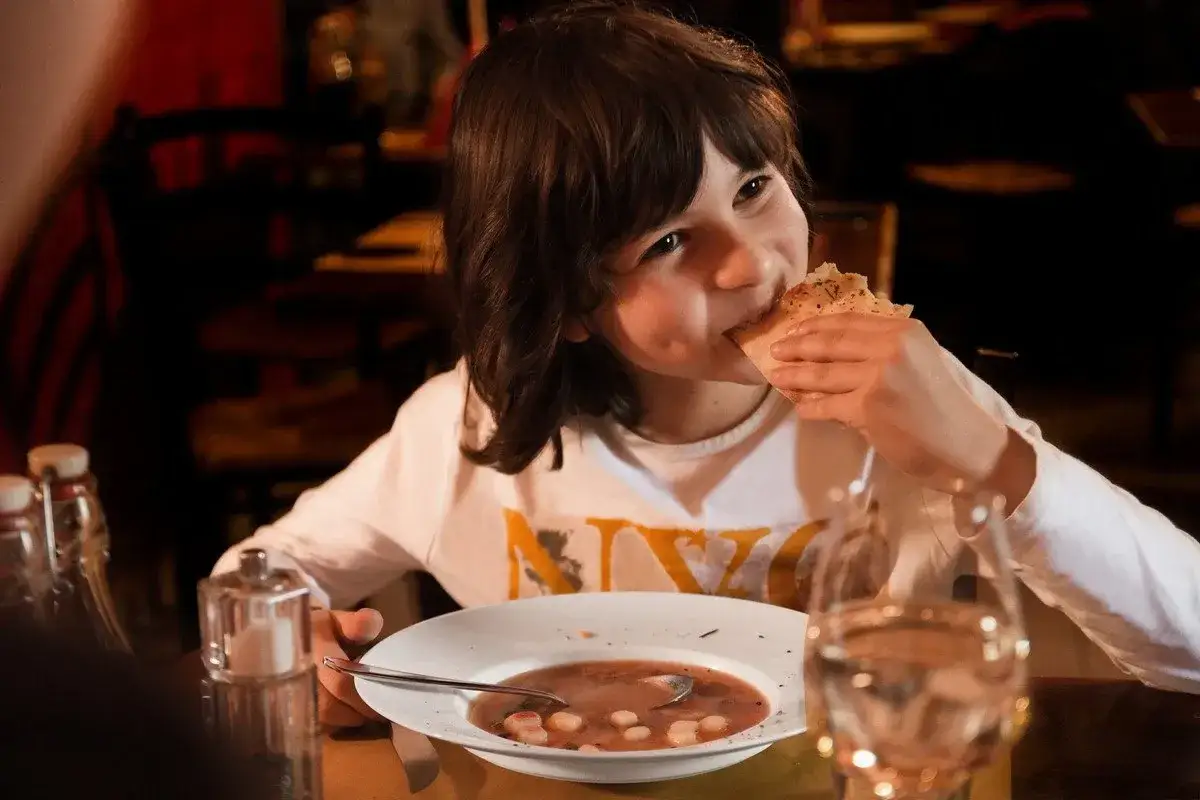 Ein Junge isst gen&uuml;sslich Brot, w&auml;hrend er eine leckere Suppe isst.