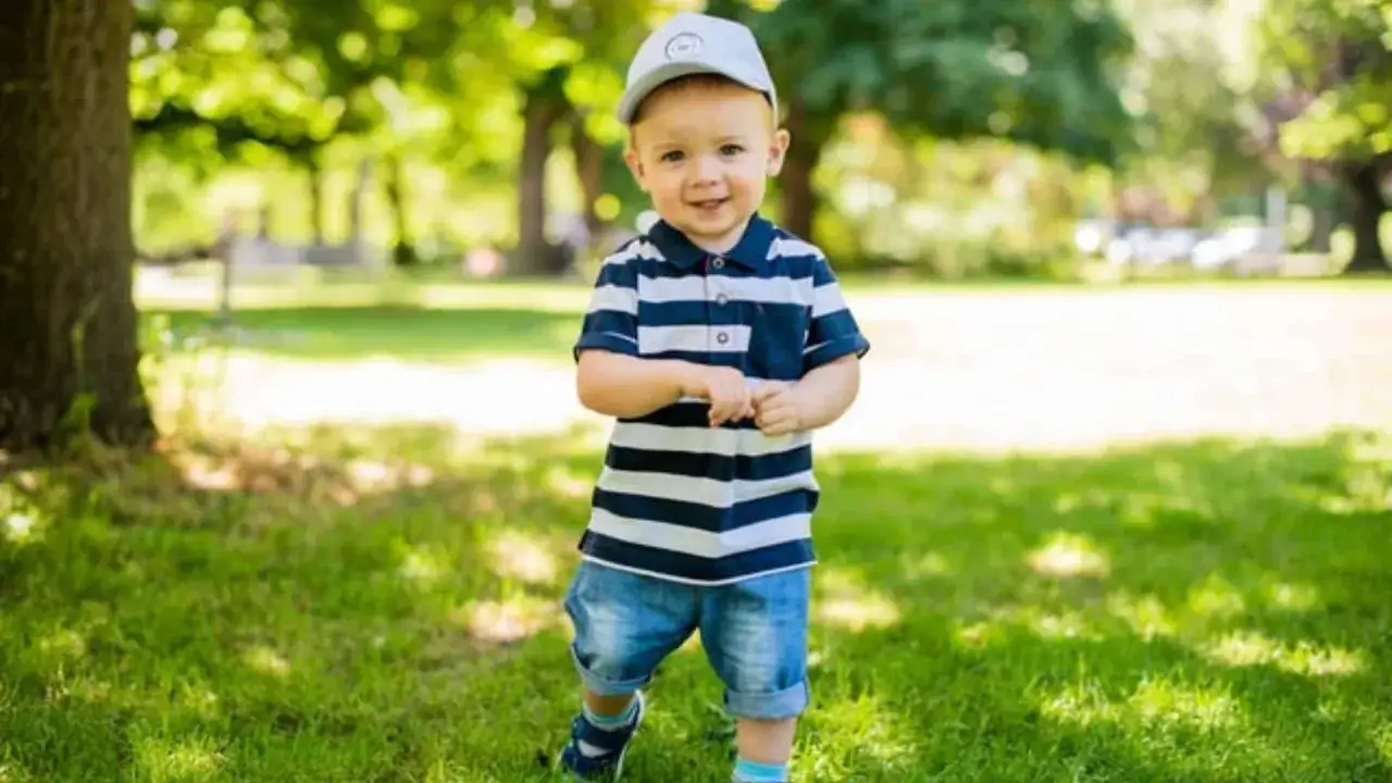 Ein fröhlicher Junge mit einem gestreiften Polo und Jeans steht im Park. Vielleicht heißt er Finn, Leo oder Noah – beliebte Jungennamen mit 4 Buchstaben.