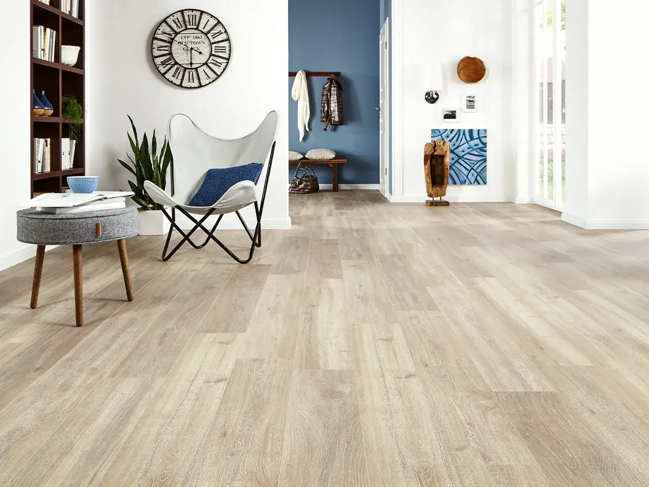 Pavimento in laminato chiaro con venature naturali, che dona calore e luminosit&agrave; all'ambiente moderno con poltrona e libreria.