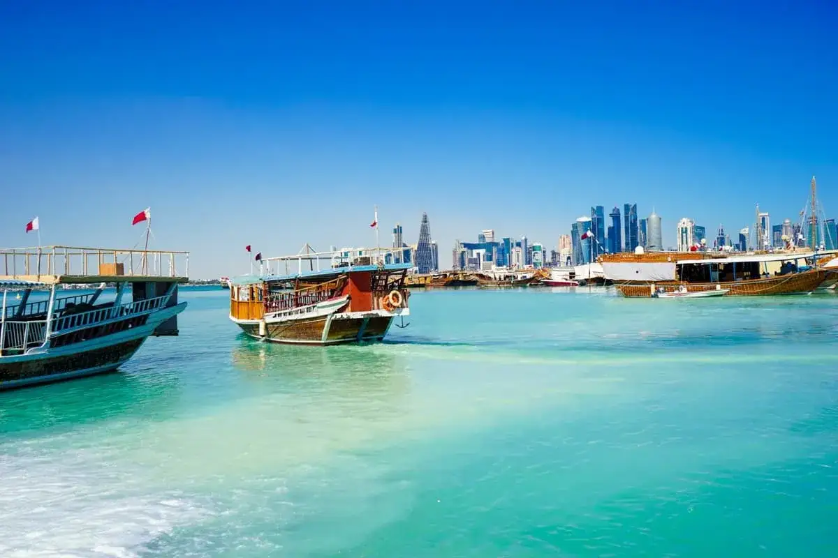 Traditionelle Dhaus-Boote im t&uuml;rkisfarbenen Wasser vor der Skyline von Doha. Ein Einblick in die katarische Kultur und maritime Geschichte.