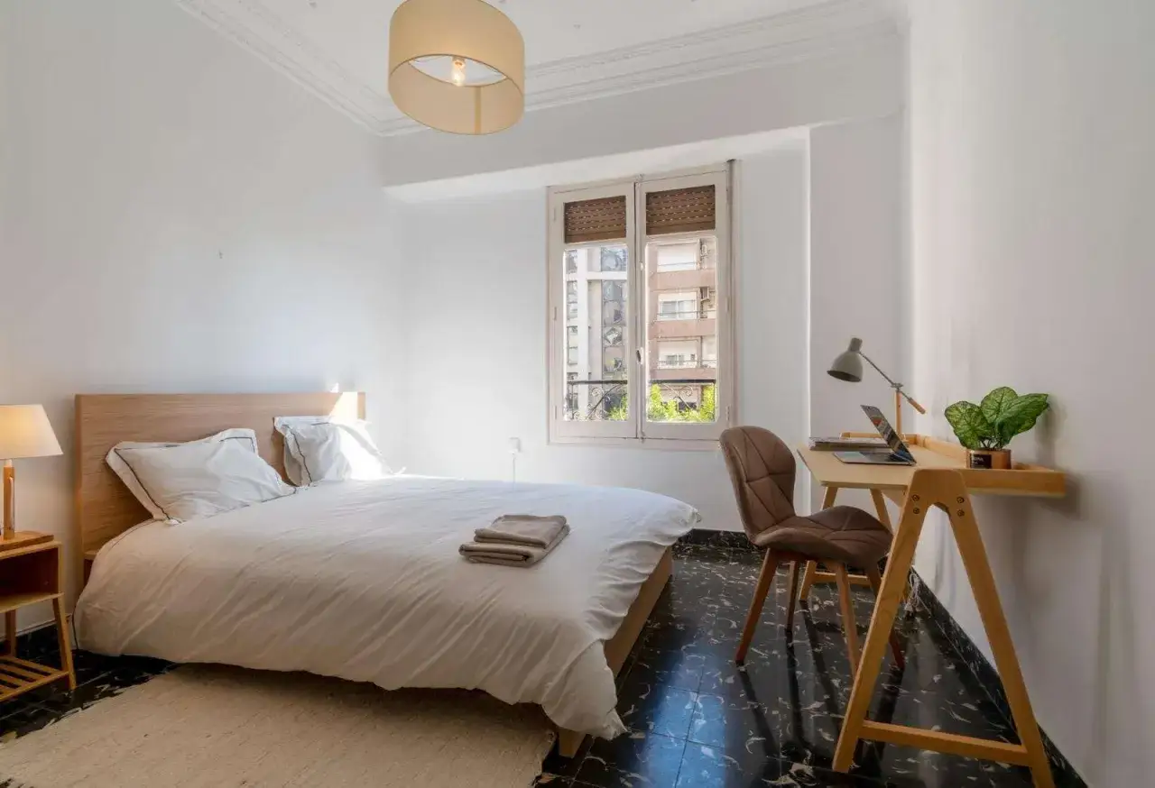Acogedora habitación de estudiante con cama, escritorio con portátil y planta. Perfecta para estudiar y descansar.