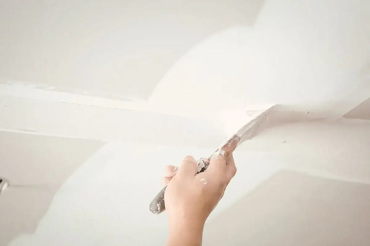 Mano aplica masilla a una pared de cal con una espátula, alisando las imperfecciones para un acabado perfecto.