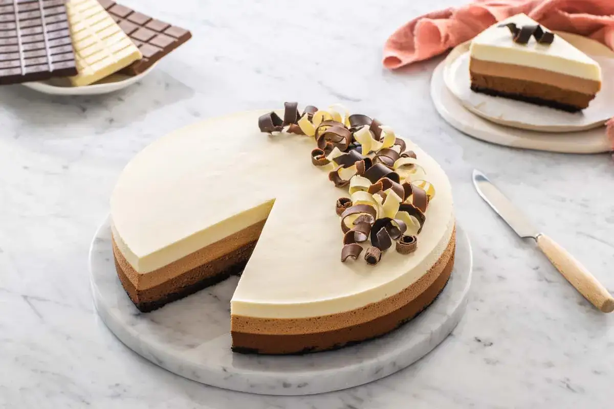Torta ai tre cioccolati ricetta facile: una delizia stratificata con cioccolato fondente, al latte e bianco, decorata con riccioli di cioccolato.