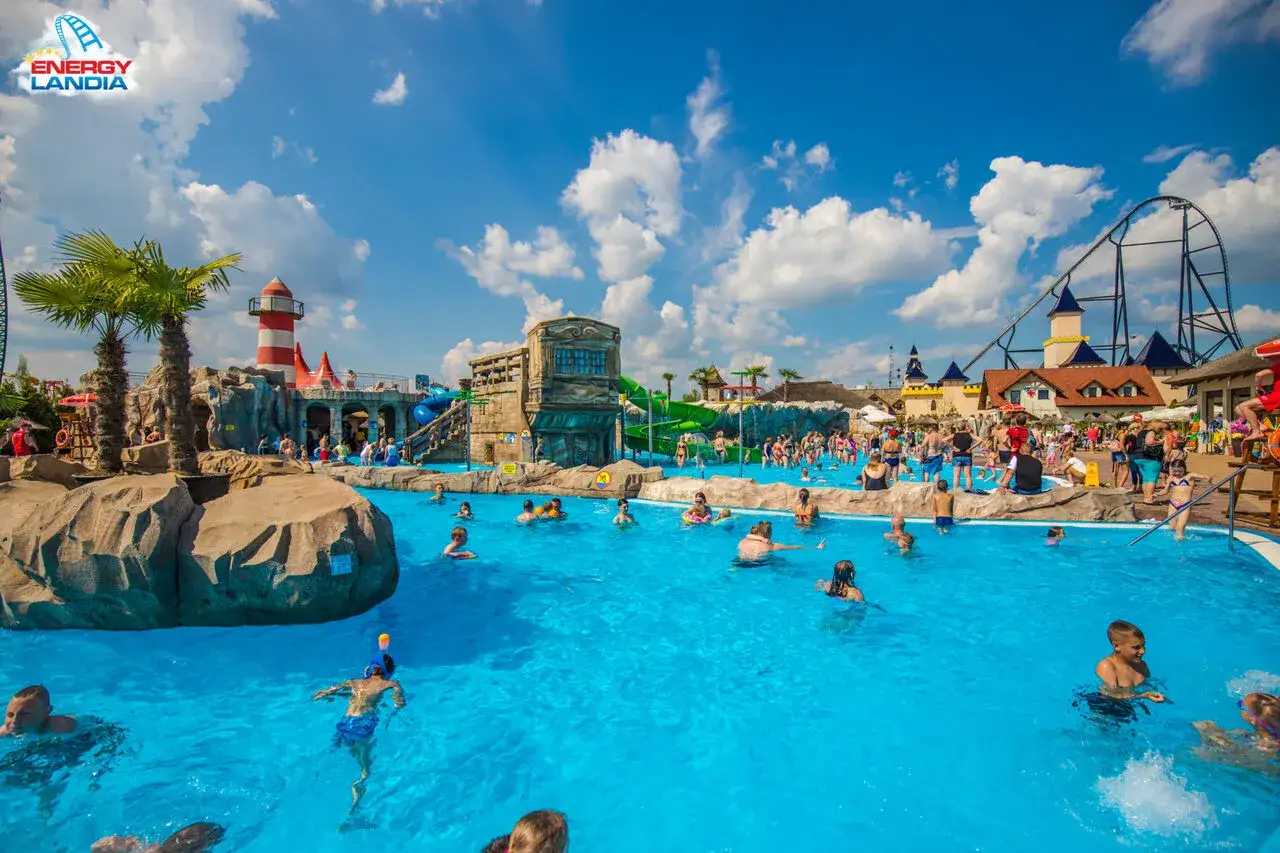 Energylandia wodne atrakcje: ludzie kąpią się w basenie, w tle zjeżdżalnie i rollercoaster.
