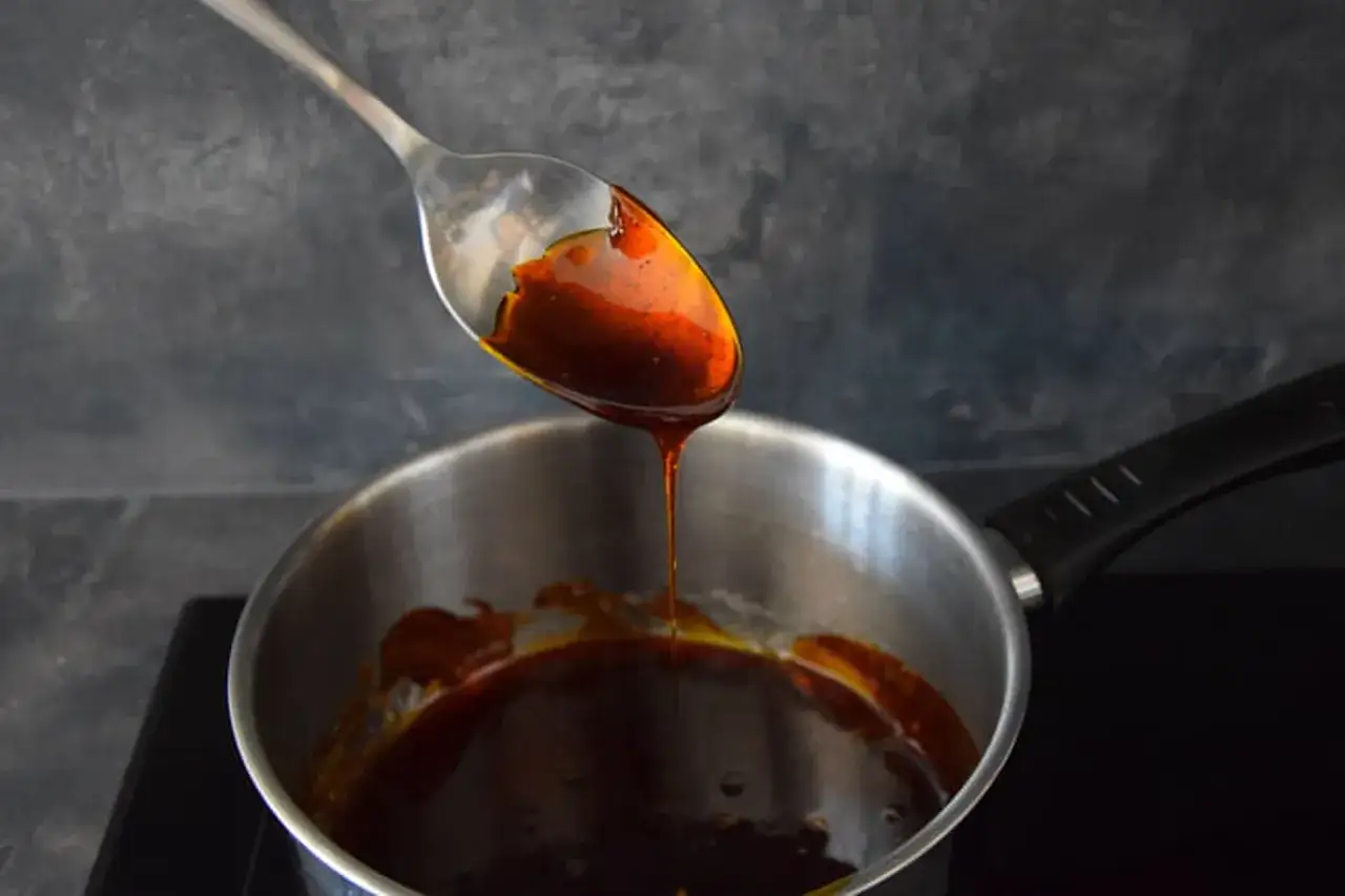 Une cuillère verse un caramel liquide doré dans une casserole. La texture sirupeuse promet une douceur gourmande.