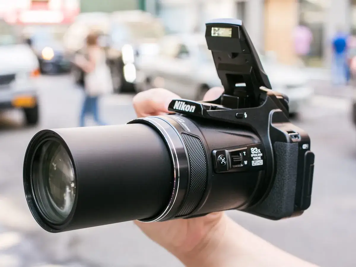 A hand holds a Nikon P90 camera with its flash up, ready to capture street scenes.