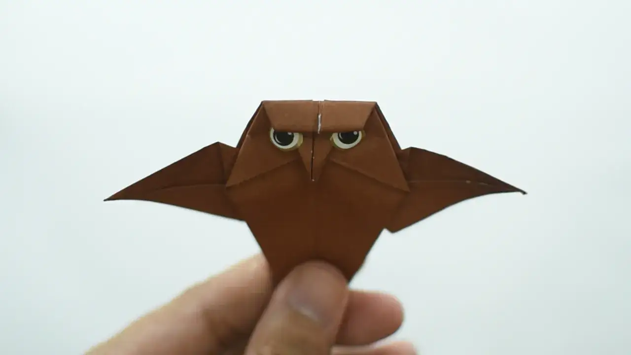Eine braune origami eule mit gro&szlig;en Augen wird von einer Hand gehalten.