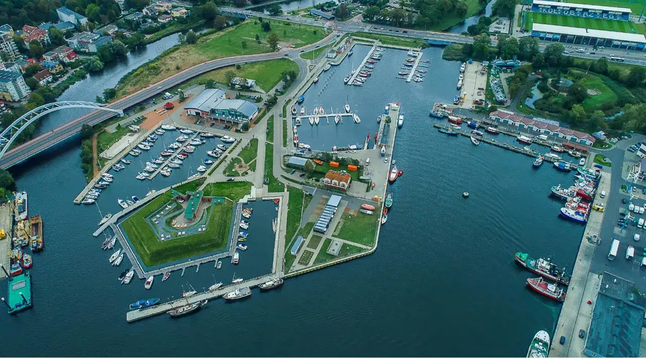 Widok z lotu ptaka na tętniący życiem port morski z licznymi jachtami i statkami zacumowanymi przy nabrzeżach.